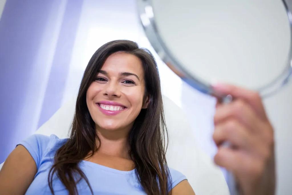 Chica mirándose al espejo después de un blanqueamiento dental